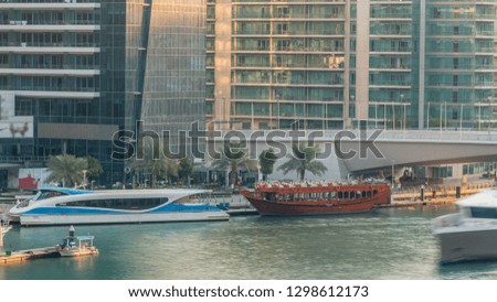 Yachts and boats with tourists staying near shoping mall and passing under a bridge in Dubai Marina district timelapse. Aerial top view at evening during sunset.