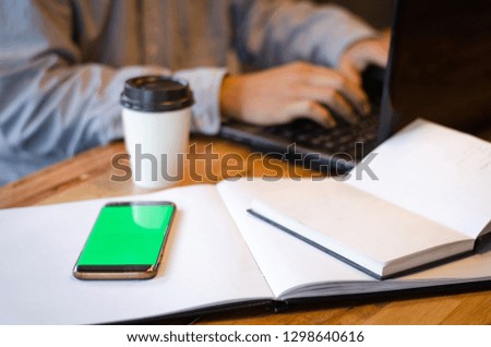 smart phone with blank green screen against man using laptop
