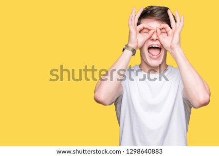 Young handsome man wearing casual white t-shirt over isolated background doing ok gesture like binoculars sticking tongue out, eyes looking through fingers. Crazy expression.