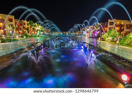 Ornate fountain water feature lit up at night by large swimming pool in a luxury tropical hotel resort