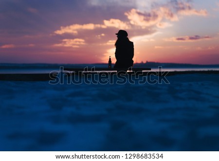 A young girl sits on a bench and drinks alcohol alone. Female alcoholism. Silhouette of a girl with a bottle. Depression.