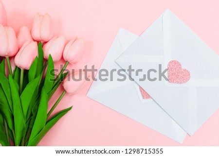 Female hands with a bouquet of pink tulips and blank white letter envelopes, on a pink background. View from above. women's Day