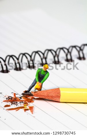 Conceptual diorama image of a miniature figure sharpening a pencil on a note book with copy space
