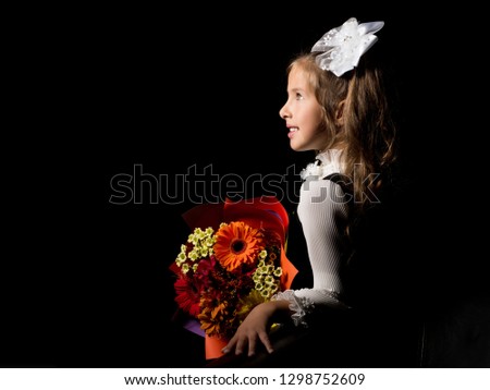 Beautiful little girl with a bouquet of flowers on a black background. The concept of a happy childhood, beauty and fashion.