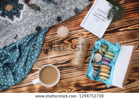 Homemade colorful macaroons in the box are lying on the brown wooden table with cup of coffee and picture Family is a gift that lasts forever. Cup of coffee. Anise, honey and colorful tissue.