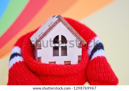 Wooden toy house in a red scarf on a rainbow colored background, warm house, insulation of house, closeup