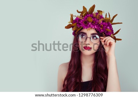 Beautiful young woman wearing floral headband in glasses isolated on light green background burgundy daisy wreath of flowers on head looking up to side smiling slightly daydreaming cute brunette girl