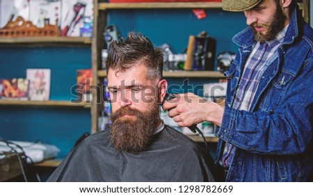 Barber with hair clipper works on hairstyle for bearded guy barbershop background. Hipster lifestyle concept. Barber with clipper trimming hair on nape of client. Hipster client getting haircut.
