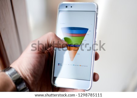 Male hand holding a smart phone showing a marketing sales funnel diagram Royalty-Free Stock Photo #1298785111