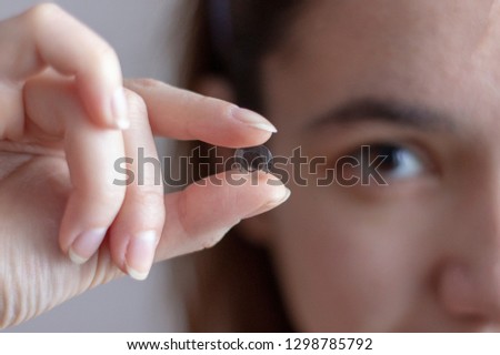 Eye lens in woman's hand with half face on the background Royalty-Free Stock Photo #1298785792