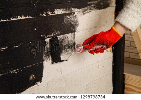 A woman in a small photo studio paints a wooden background with black paint