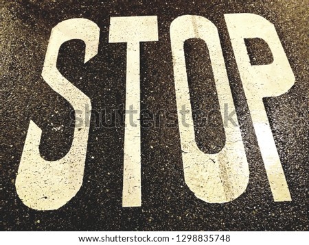 CLOSE UP OF A WARNING SIGN WITH THE LETTERS STOP IN WHITE ON WET BLACK ASPHALT OT THE STREET MEANING TO STOP THE VEHICLE AT THE URBAN ROAD. HORIZONTAL PHOTO