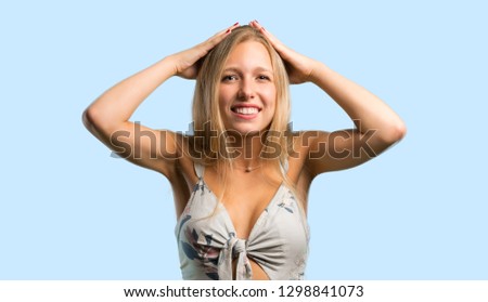 Young blonde woman takes hands on head because has migraine on blue background