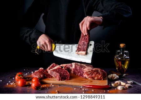 Butcher cuts fresh meat on the wood board.Beef steak and salt on background with free space for text design or logotype menu restaurant.  Royalty-Free Stock Photo #1298849311