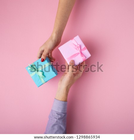 man and girl exchanging gifts from hand to hand,boxes wrapped in decorative paper with a bow on pastel pink background, the concept of holidays and love , top view