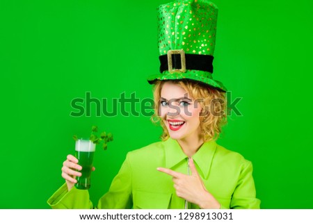 Saint Patrick. Green top hat. St Patricks Day. Woman in top hat points at glass with beer. Leprechaun. Green beer. Green hat with clover. Irish Traditions. Pub. Woman drinking in pub. Irish beer. Royalty-Free Stock Photo #1298913031