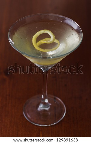 dirty martini chilled and served on a busy bar top with a shallow depth of field and color lights and glasses in the background garnished with a lemon twist