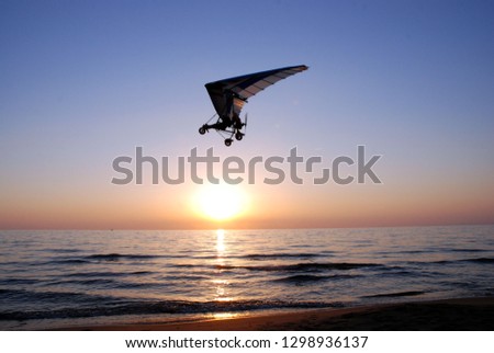 ultralight trike flies making evolutions and low passes on the beach on sunset at the end of summer Royalty-Free Stock Photo #1298936137