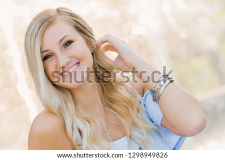 One attractive blonde hair caucasian high school senior posing for senior pictures. Female Teenager portrait outdoors at park in summer.