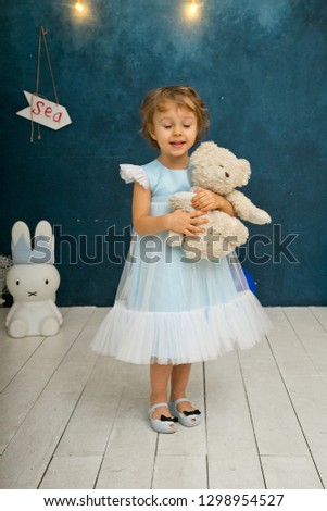 girl in a blue dress with a teddy bear and blue balls in their hands
