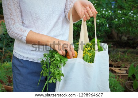 Asian woman add orange into tote bag with green garden background.Use tote bag for Replacement plastic bag can save the earth.Zero Waste, Healthy Eating, Package Free,Green Living concept. Royalty-Free Stock Photo #1298964667