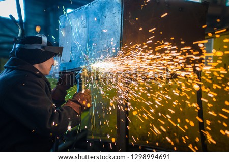 A man in working form and a face mask cuts a metal saw with a Bulgarian on the background of a metallurgical industrial plant.
