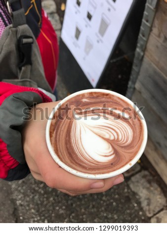 Cappuccino coffee with a picture of a take-out heart in a glass in the hands, Top view