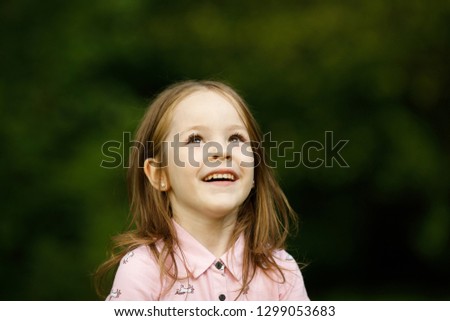 Emotional portrait of a happy and positive little girl looking with a smile at the birds on the background of blurred foliage on a walk in the park.Happy childhood. Positive emotions and energy.Summer