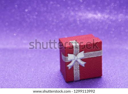 Red gift box on purple sparkling background.
