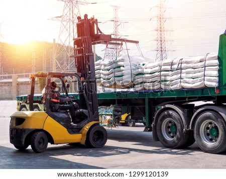 Forklift handling white sugar bags from warehouse for stuffing into a truck outdoors. Royalty-Free Stock Photo #1299120139