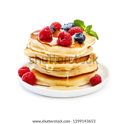 Delicious pancakes with berries, honey or maple syrup. Homemade pancakes and sweet syrup on white plate isolated.