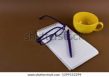 still life with yellow cup, glasses,pen  and opened notebook with empty sheet