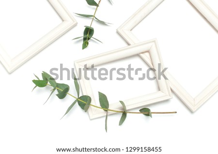 White wooden photo frame and green eucalyptus leaves on white background. Flat lay top view copy space. Stylish minimal composition, artwork mockup, picture frame, home decoration
