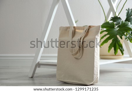 Eco bag and houseplant near white wall indoors. Space for design