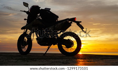 Silhouette motorcycle with helmet and bag against sunset background.