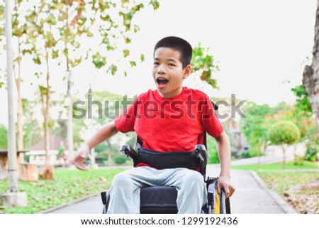 Child sitting on wheelchair is enjoying activities in the park like other people. Happy disabled kid concept.