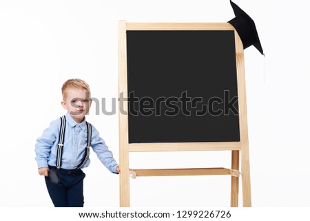 Child back to school and educational concept. Portrait of graduate little boy near  the chalk board and  black graduation hat. Isolated on white background. 
