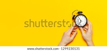 Flat lay top view male hand holding black vintage alarm clock on bright yellow color background with copy space. Creative Time concept minimal style, morning time to work