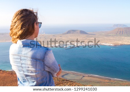 A girl stands turned backs against the background of the Atlantic Ocean and the island of La Graciosa. Mountain. Mirador del Rio. North of Lanzarote. Canary Islands. Spain