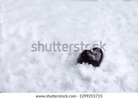 Assorted milk and dark chocolate heart on snow with copy space, Black Valentine's Day concept.