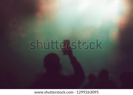 Blurred background with black silhouette of concert fan taking pictures with smart phone in bright green and yellow stage lights