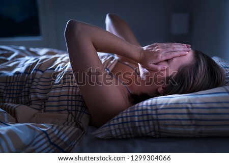 Insomnia, sleep apnea or stress concept. Sleepless woman awake and covering face in the middle of the night. Lady can't sleep. Nightmares or depression. Suffering from headache or migraine.  Royalty-Free Stock Photo #1299304066