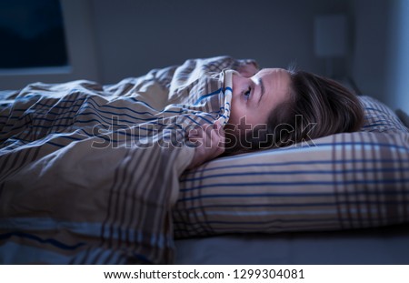 Scared woman hiding under blanket. Afraid of the dark. Unable to sleep after nightmare or bad dream. Awake in the middle of the night in bedroom at home.  Monster under the bed or in closet. 
 Royalty-Free Stock Photo #1299304081
