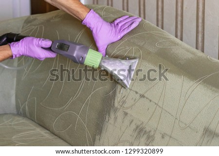 Closeup of upholstered Sofa chemical cleaning with professional extraction method.  Man hands in rubber gloves hold hoover nozzle Royalty-Free Stock Photo #1299320899