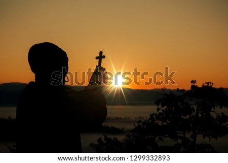 Silhouette of human hand holding the cross, the background is the sunrise., Concept for Christian, Christianity, Catholic religion, divine, heavenly, celestial or god.