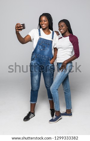 Portrait of two african young girls taking selfie on smartphone isolated over white background