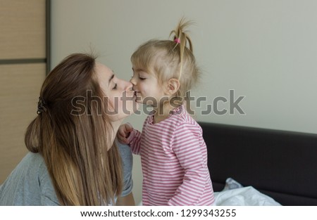 family, children and happy people concept - happy little girl  kissing her mother on the bed at home.