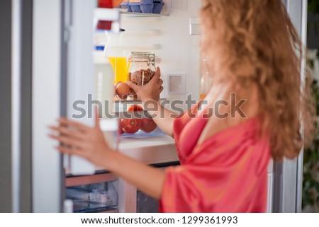 Woman standing in front of fridge full of groceries and taking jar. Morning routine.
