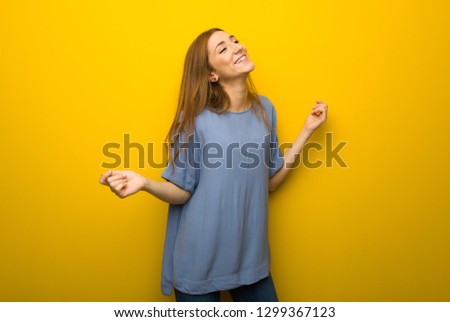 Young redhead girl over yellow wall background enjoy dancing while listening to music at a party