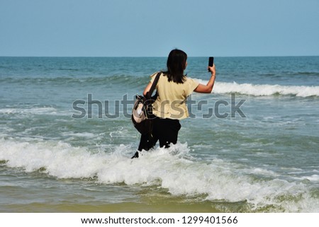 A woman is taking picture wave and sea with her smart phone on the beach in her holiday